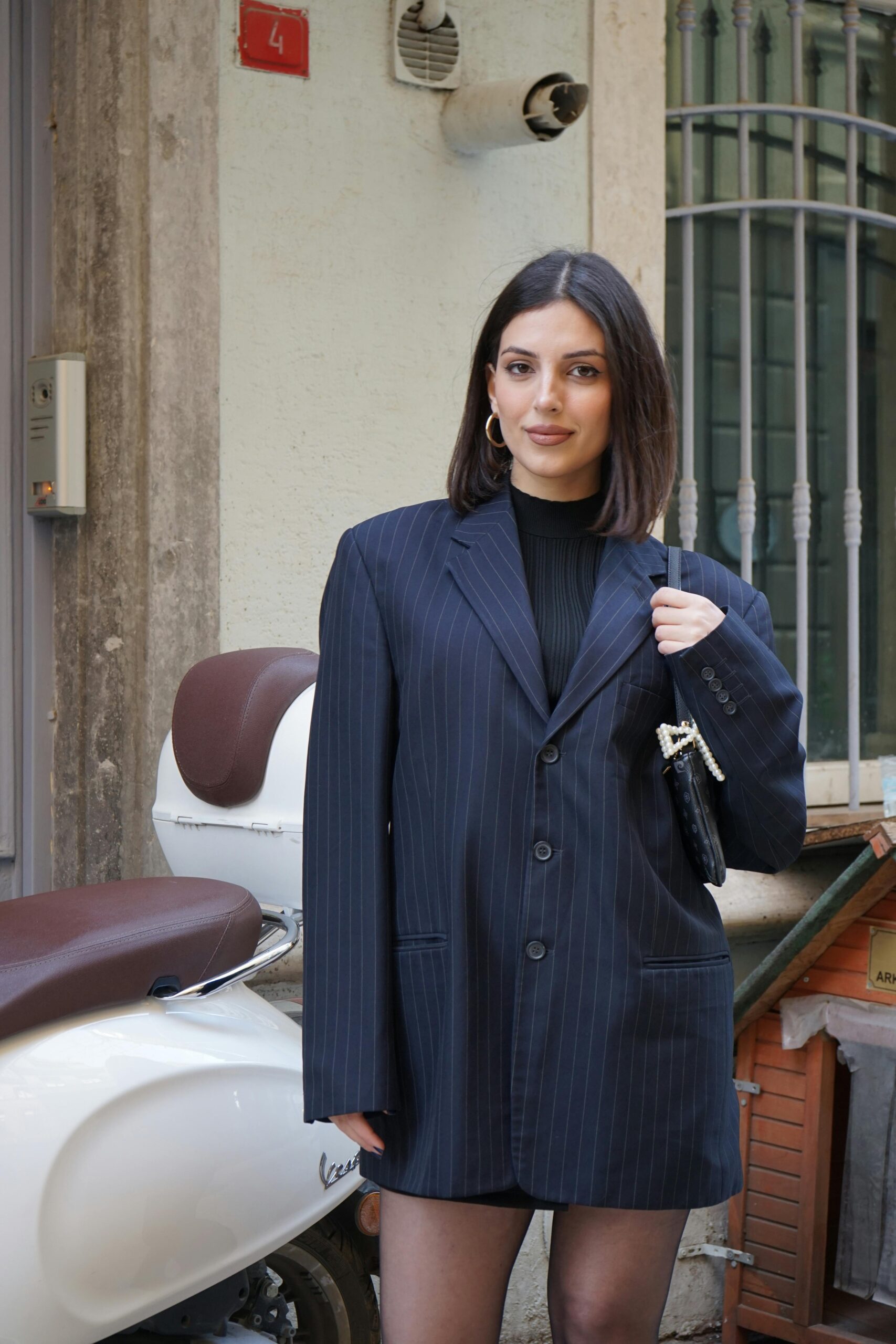 Elegant woman in a pinstripe suit jacket stands confidently in an urban setting.